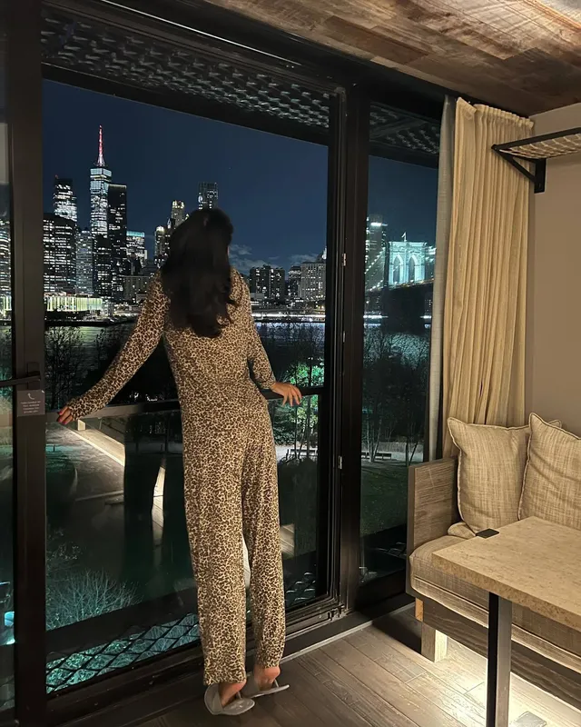 Greta Onieogou posing in a patterned outfit and clear heels beside a window.