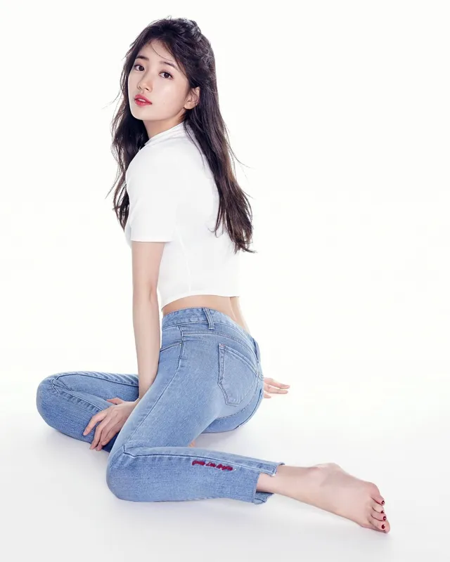 Bae Suzy sitting barefoot in jeans and a white top.