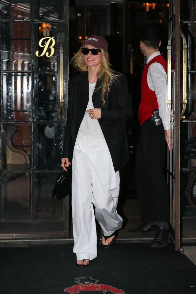 Olivia Wilde walking outdoors in white trousers and flip-flops.