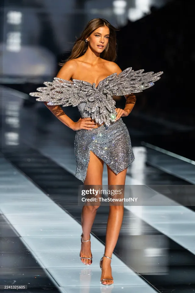 Barbara Palvin walking a runway in a sparkling outfit and heels.