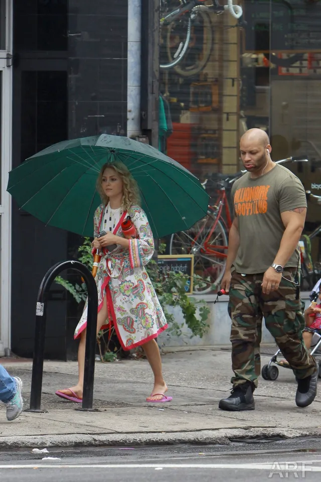 AnnaSophia Robb walking with a companion beneath a green umbrella.