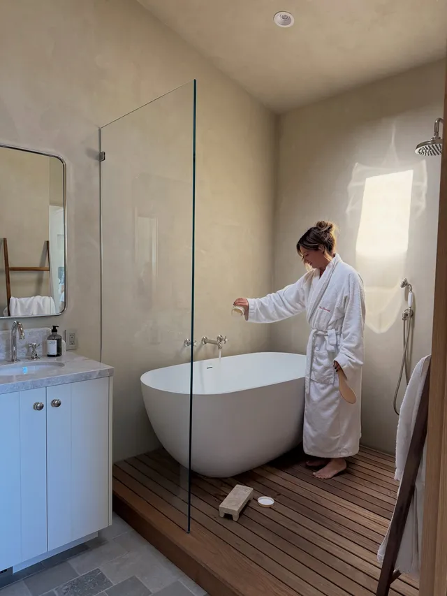 Ashley Tisdale standing barefoot in a robe beside a bath.
