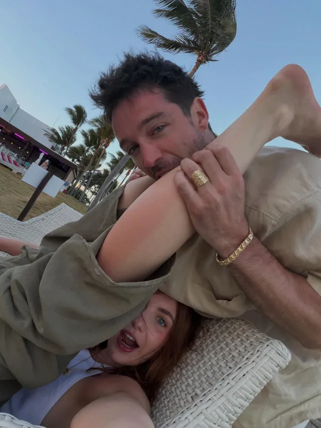 Sophie Nélisse raising a bare foot beside a man on a sun lounger.