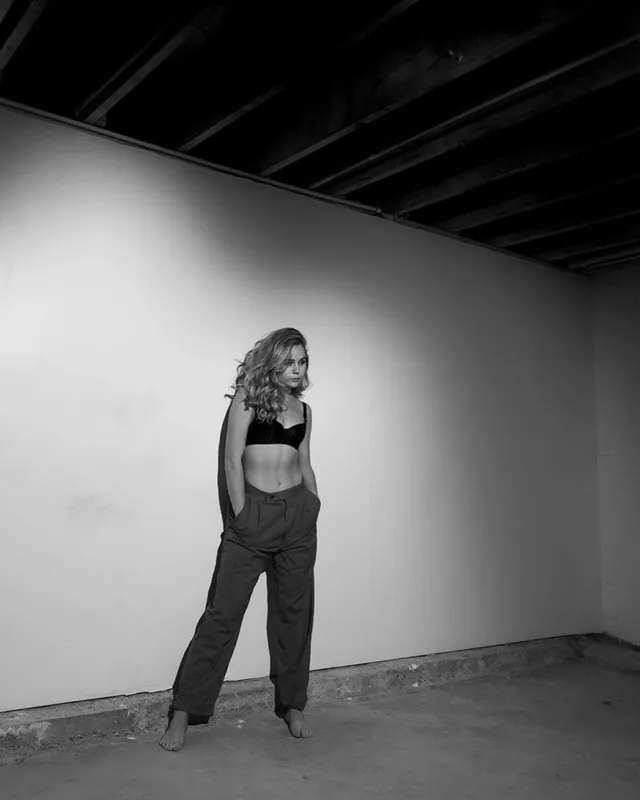 Brec Bassinger posing barefoot in a dark outfit for a monochrome portrait.