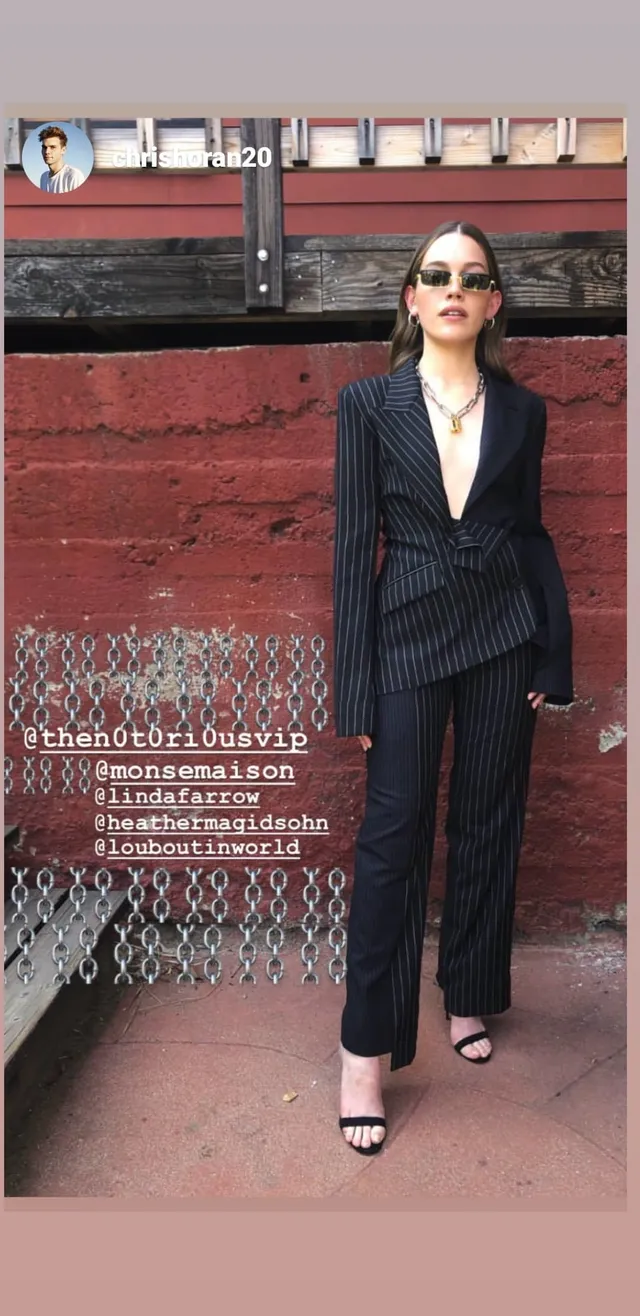 Victoria Pedretti standing outdoors in a dark suit.