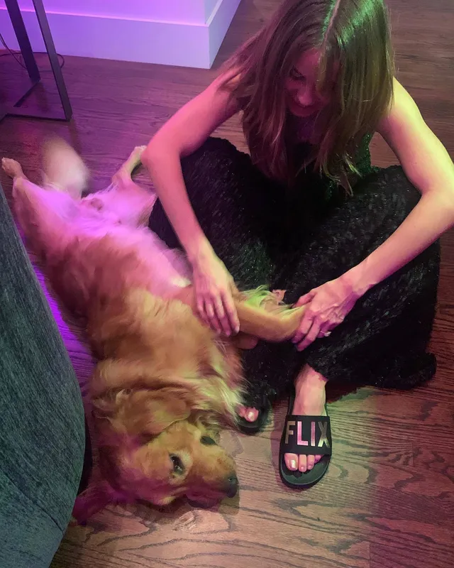 Debby Ryan sitting indoors in a black outfit beside a dog.