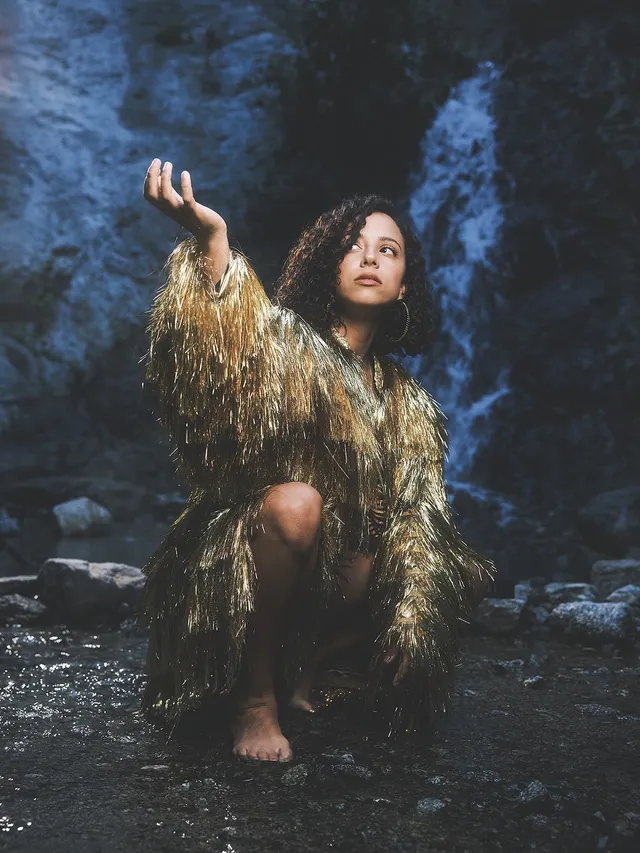 Kiana Madeira posing barefoot in a patterned outfit beside a waterfall.