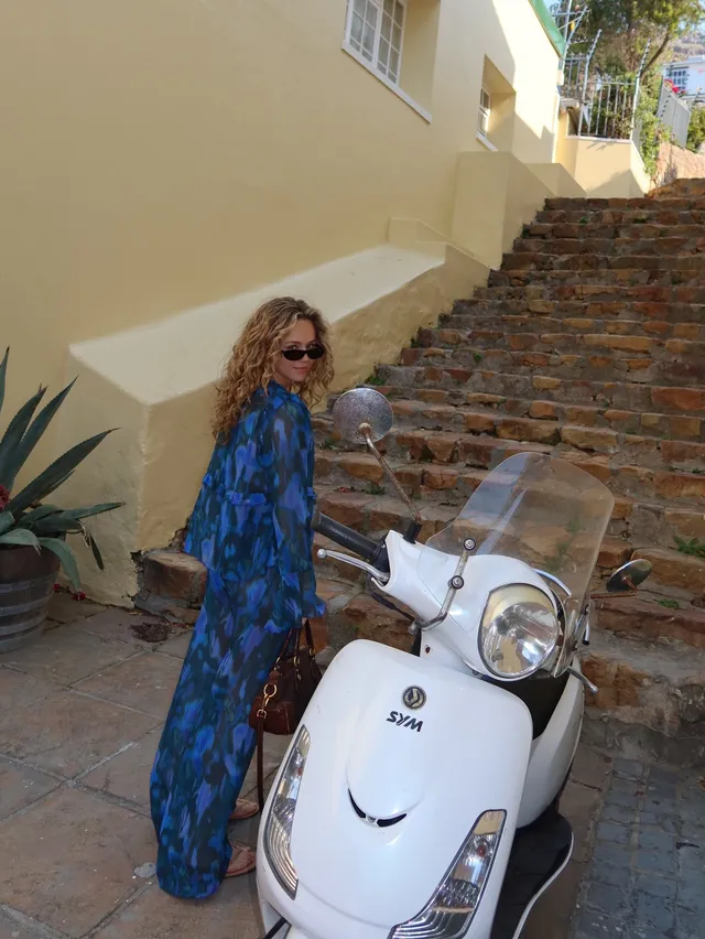 Brec Bassinger standing beside a scooter in a long blue dress.