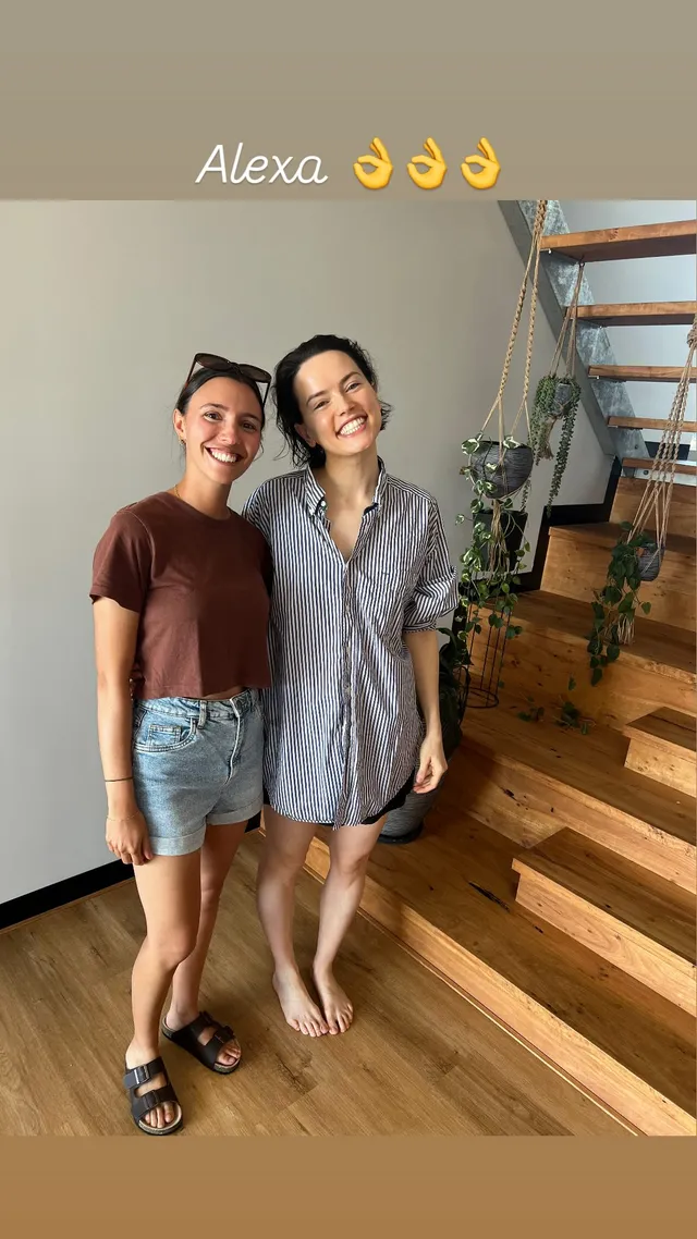 Daisy Ridley standing with a friend beside a staircase.