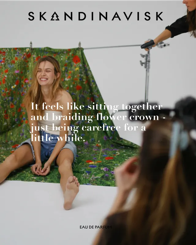 Josephine Skriver sitting barefoot in front of a floral backdrop during a fragrance shoot.