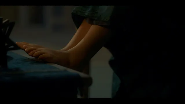 Olivia Cooke resting her feet on a seat in a dimly lit scene.