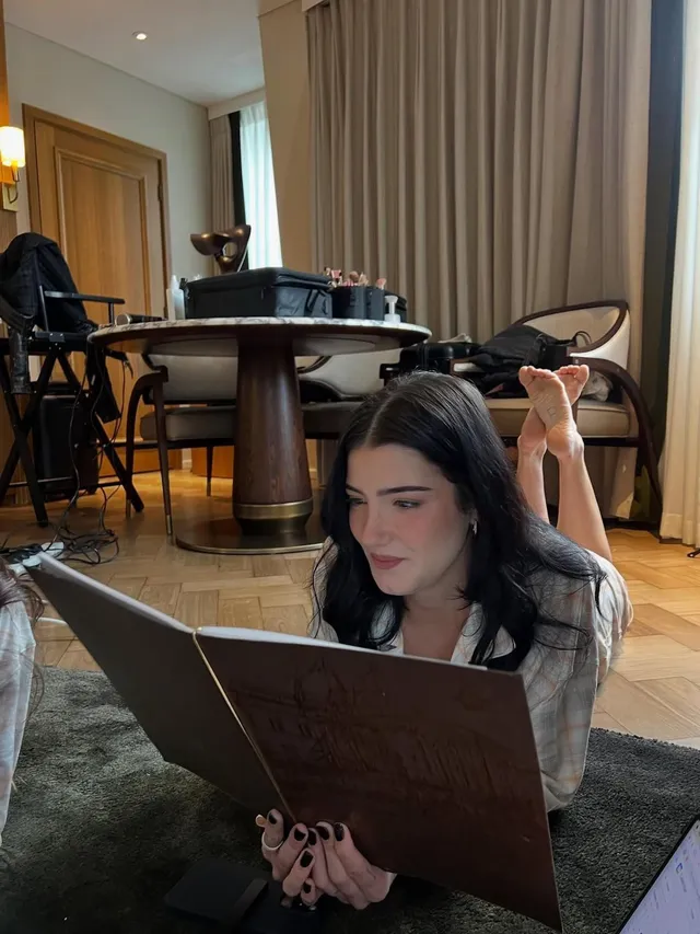 Charli D’Amelio lying on a rug with bare feet raised while reading.