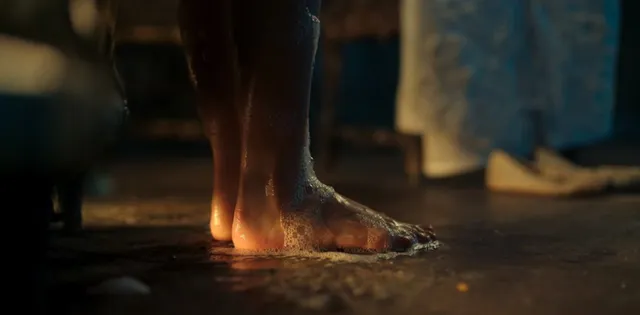 Freya Allan standing barefoot on a damp floor in a film scene.