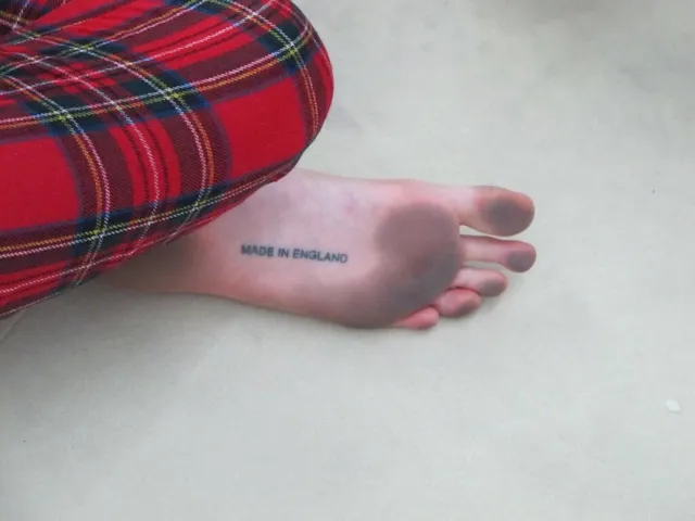 Cara Delevingne resting a tattooed foot beside patterned trousers.
