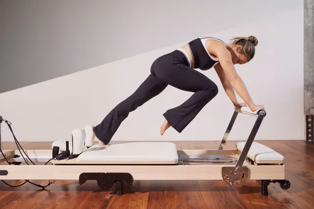 Hilary Duff exercising barefoot on a Pilates reformer in side view.