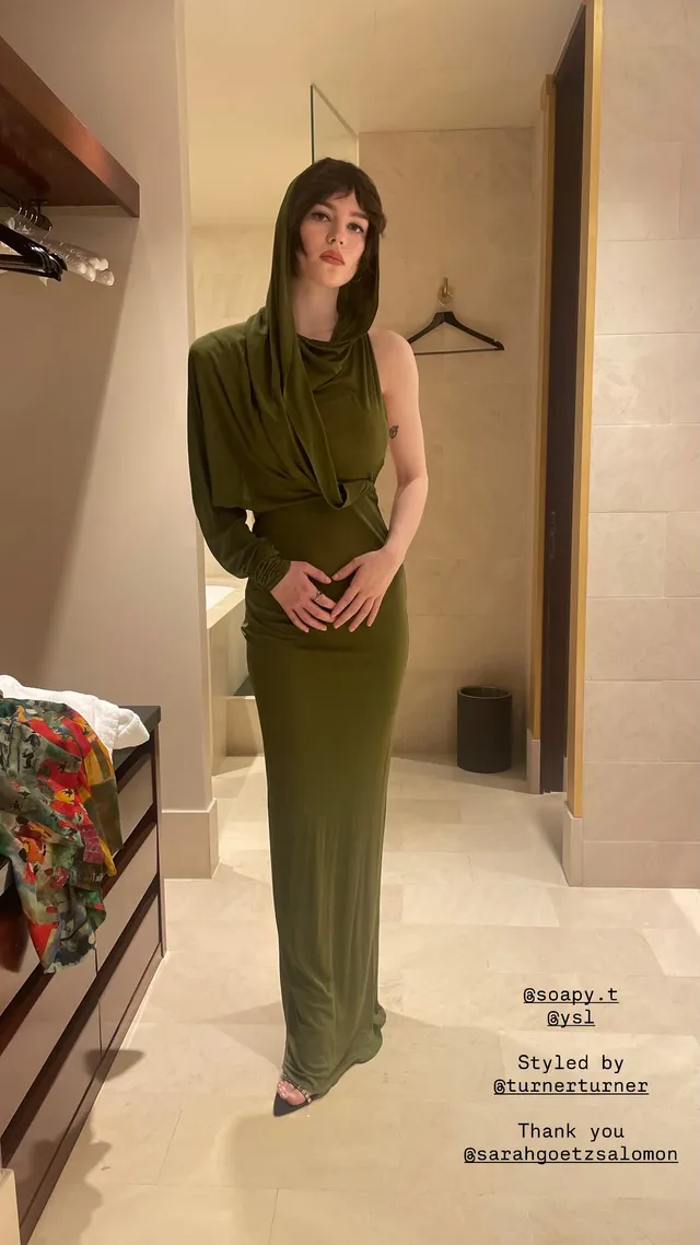 Sophie Thatcher posing in a long green dress and open-toe heels.