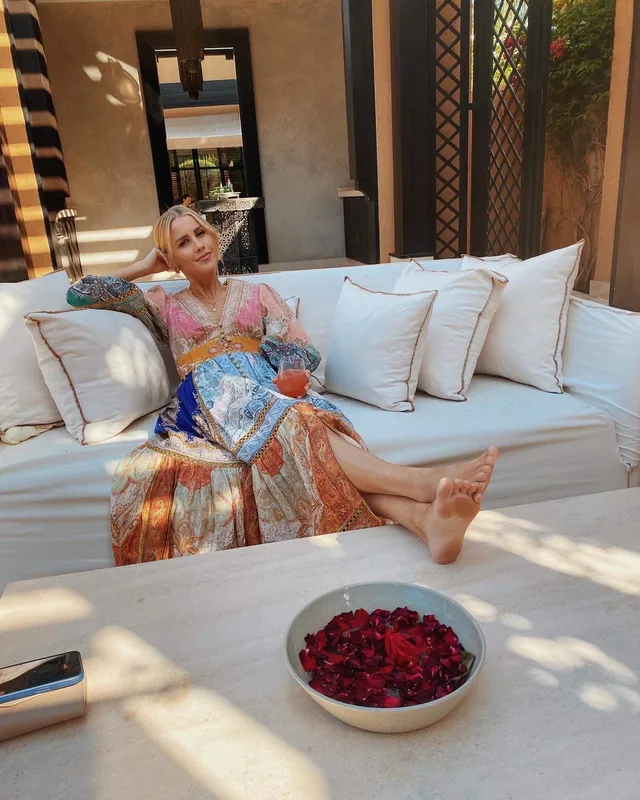 Claire Holt relaxing on an outdoor sofa in a colorful dress.