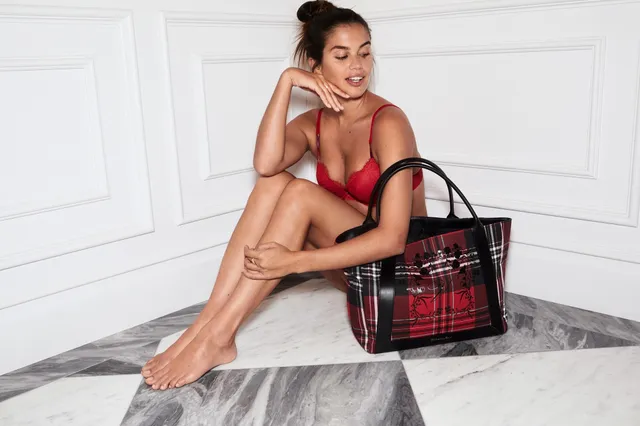 Sara Sampaio sitting barefoot beside a patterned handbag in a red outfit.