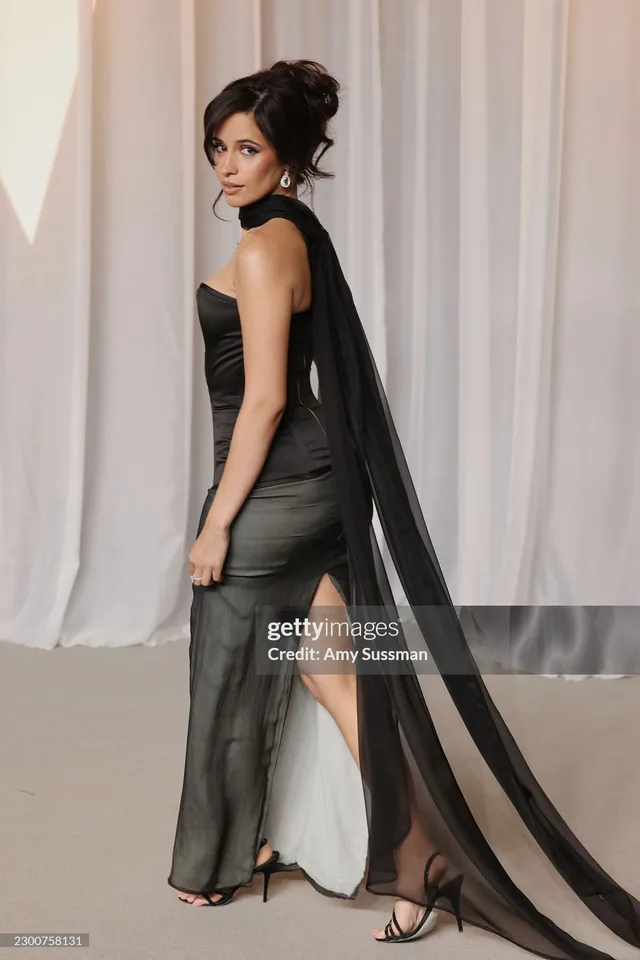 Camila Cabello posing in a black gown beside white curtains.