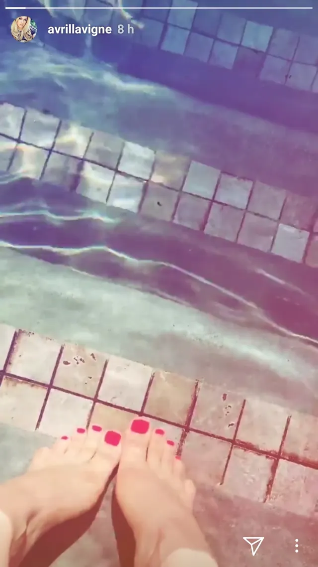Avril Lavigne standing barefoot beside a tiled swimming pool.