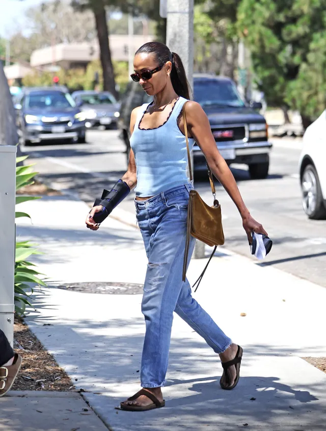 Zoe Saldaña walking outdoors in jeans and flat sandals.