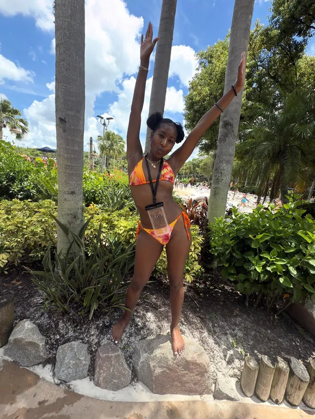 Carlacia Grant posing barefoot in a colorful bikini among palm trees.