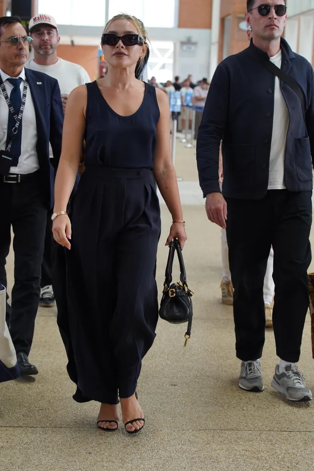 Florence Pugh walking in a navy jumpsuit and strappy heels.