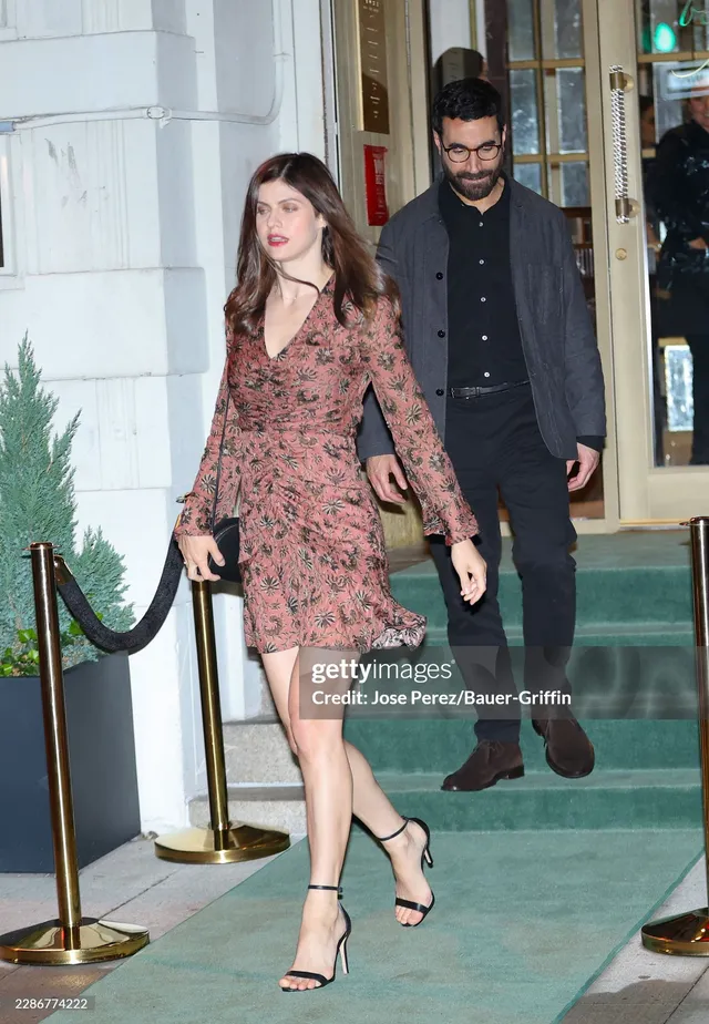 Alexandra Daddario walking in a patterned dress with black heels.