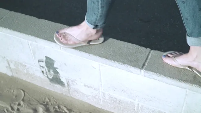 Elisha Cuthbert wearing pale flip-flops beside a pavement.