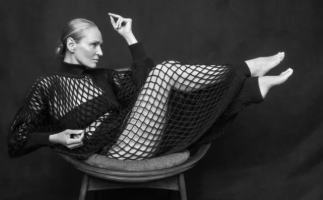Uma Thurman reclining barefoot in a black outfit and patterned tights.