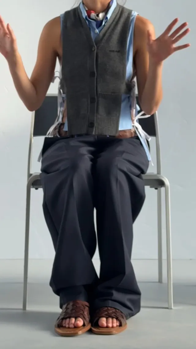 Olivia Rodrigo sitting in a chair wearing wide leg trousers and heeled sandals.