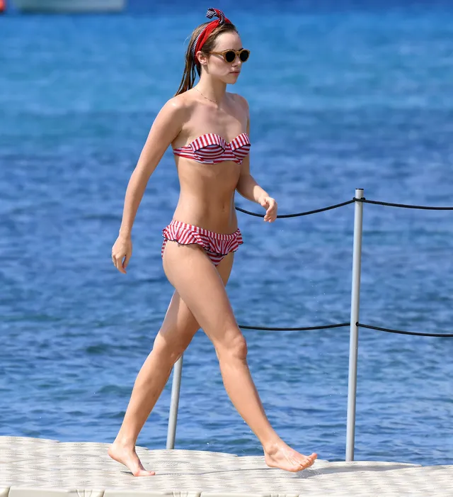Suki Waterhouse walking along a seaside path in a red headband.