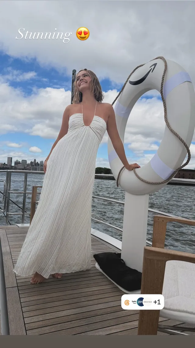 Bailee Madison standing barefoot in a white dress beside a life ring.