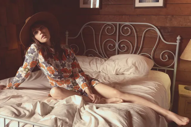 Felicity Jones reclining on a bed in a patterned dress.