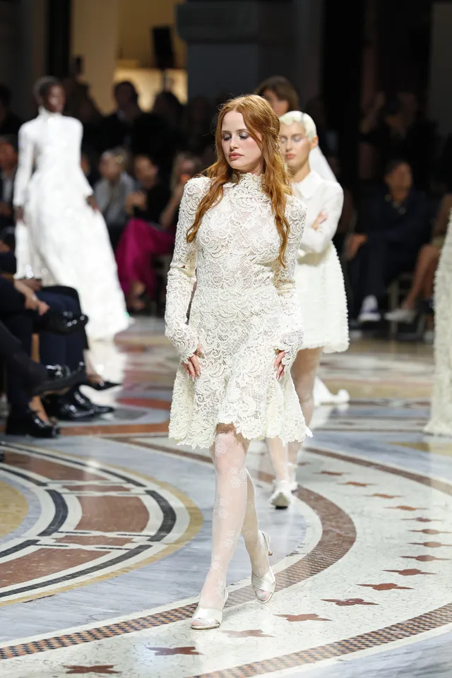Madelaine Petsch walking in a white lace outfit and pale heels.