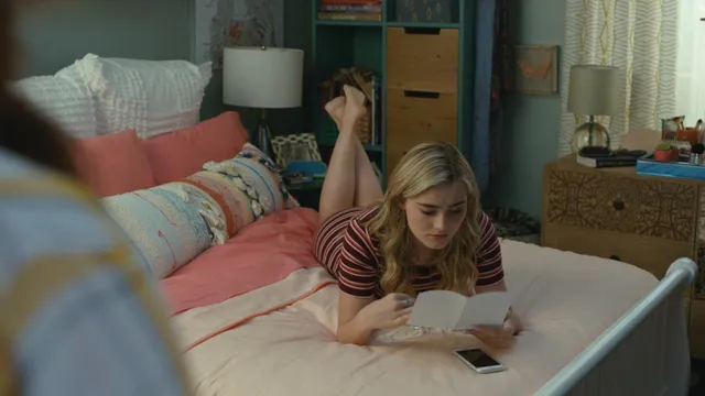Meg Donnelly lying barefoot on a bed in a striped top in a scene.