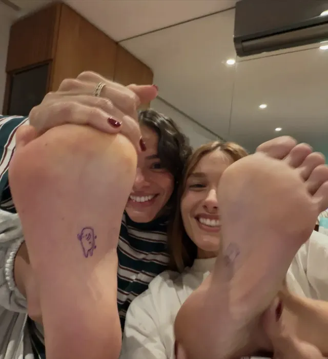 Bruna Marquezine posing with a friend with bare feet raised toward the camera.