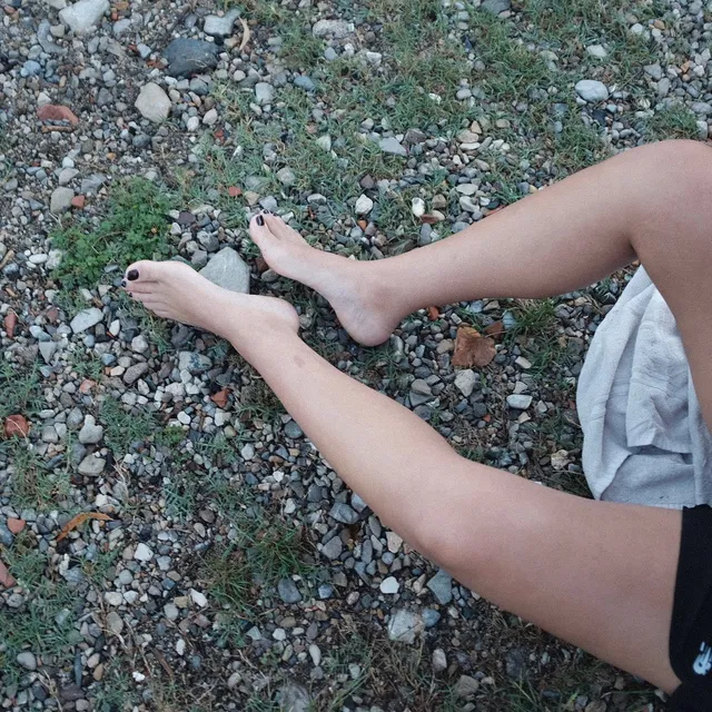 Naomi Scott resting bare feet on a pebbled beach.