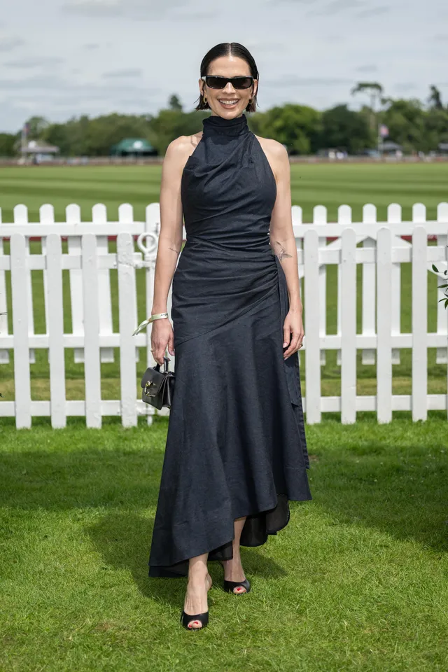 Hayley Atwell posing beside a white fence in a black dress.