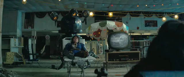 Ella Purnell sitting in a workshop setting in a screen scene.