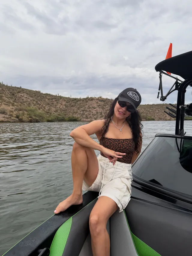 Vanessa Hudgens sitting barefoot aboard a boat in a cap and white shorts.