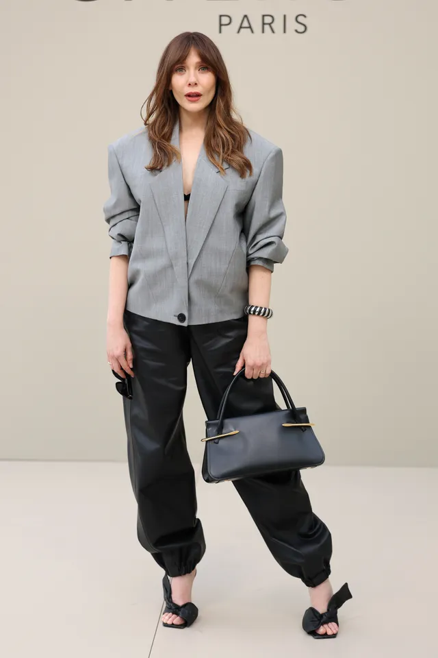 Elizabeth Olsen posing in a gray jacket and black heels.