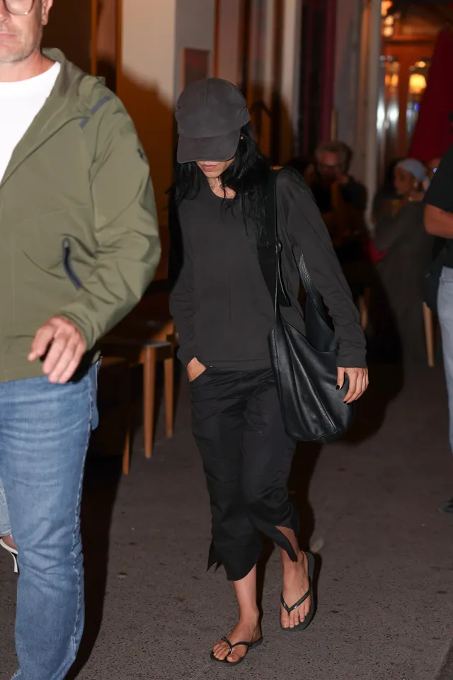 Jenna Ortega: standing outdoors in a black outfit and flip-flops.