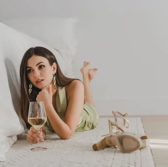Victoria Justice lying barefoot on a rug in a pale green dress.