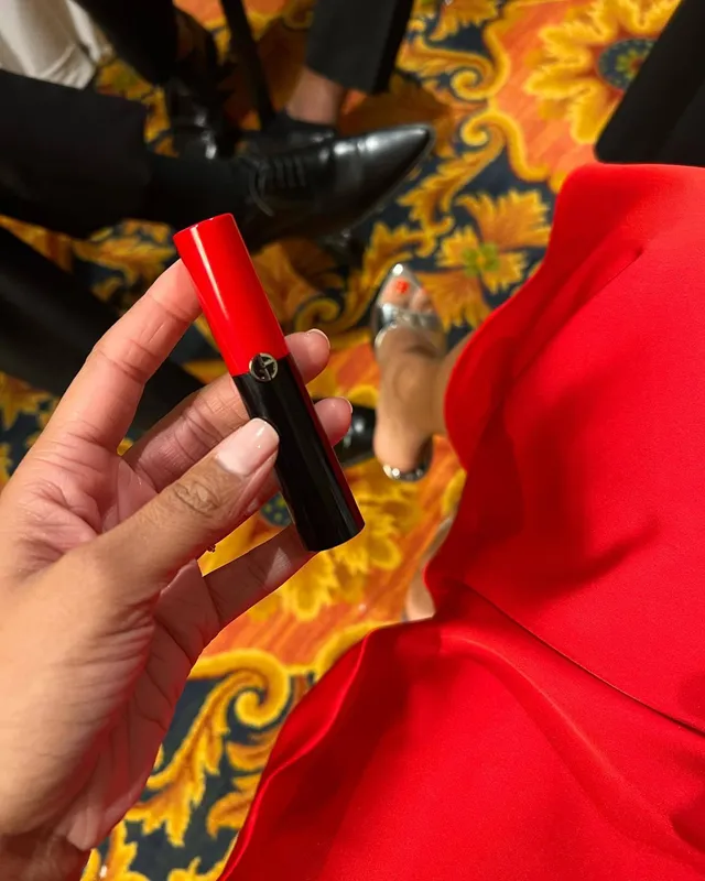 Greta Onieogou shown from above in a red outfit and clear heels while holding lipstick.