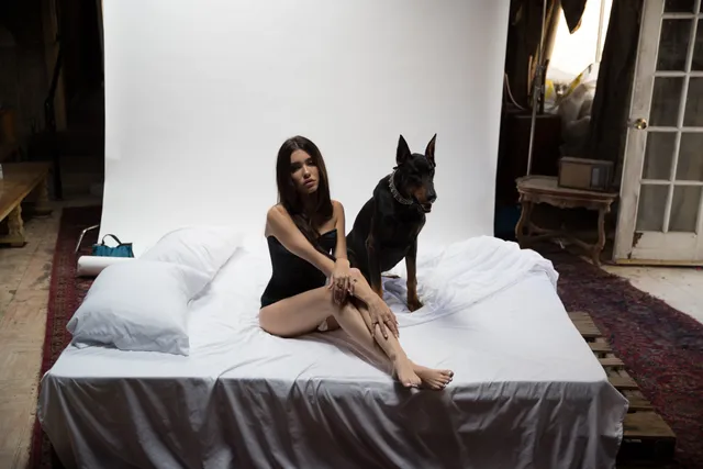 Madison Beer: seated barefoot on a white bed beside a dog.