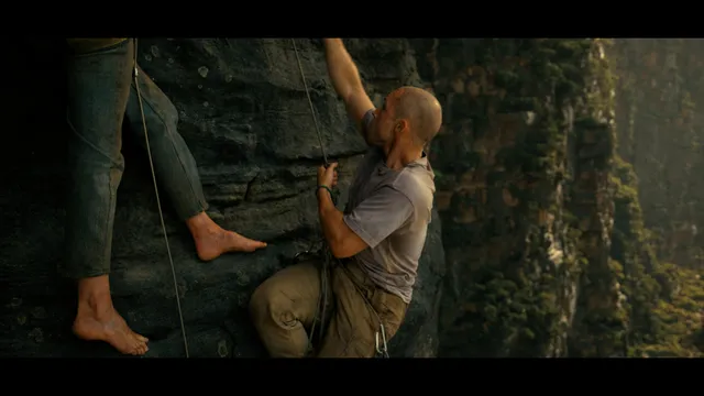 Charlize Theron a screen scene climbing beside a rock face.