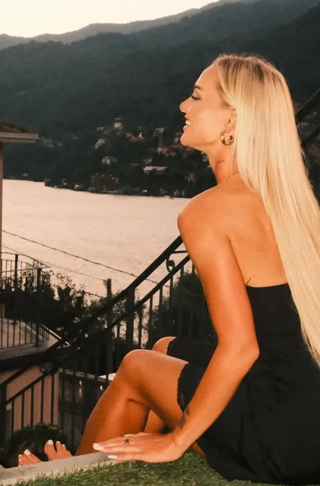 Alisha Lehmann sitting barefoot on an outdoor ledge in a black dress.