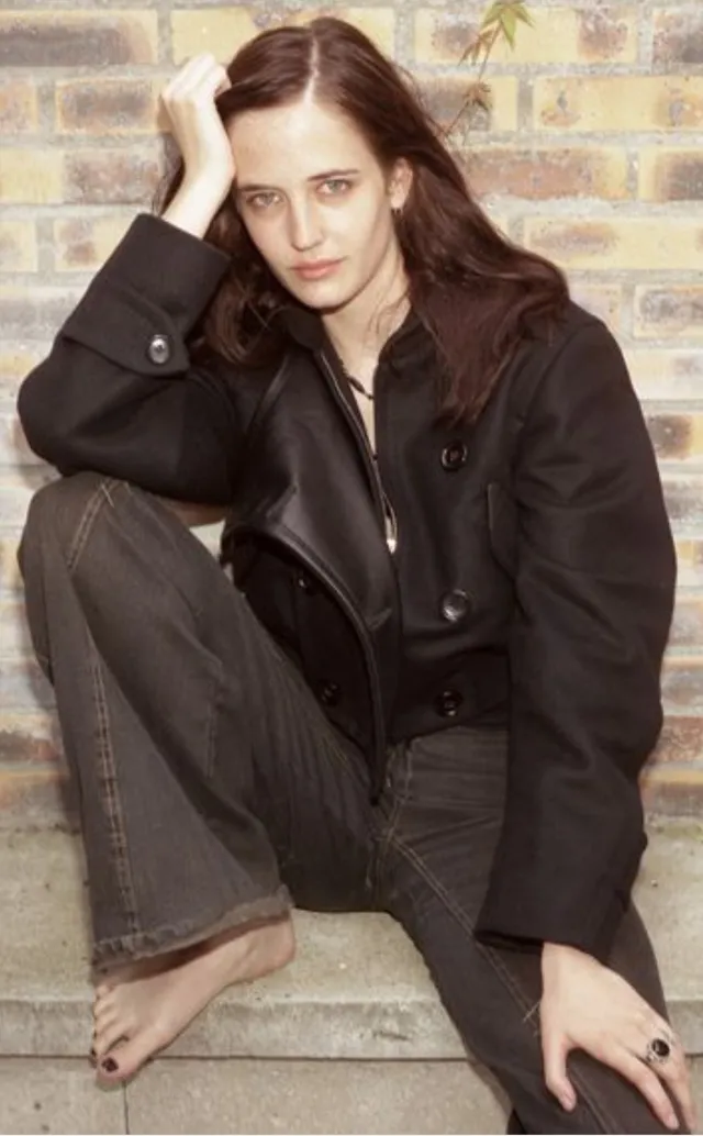 Eva Green seated on stone stairs in dark trousers.