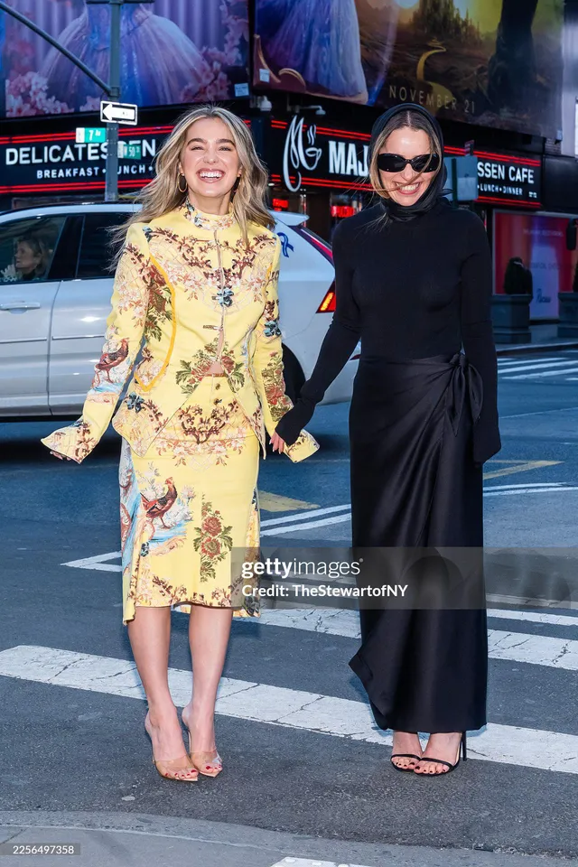 Emilia Clarke walking outdoors in black trousers and open-toe heels.